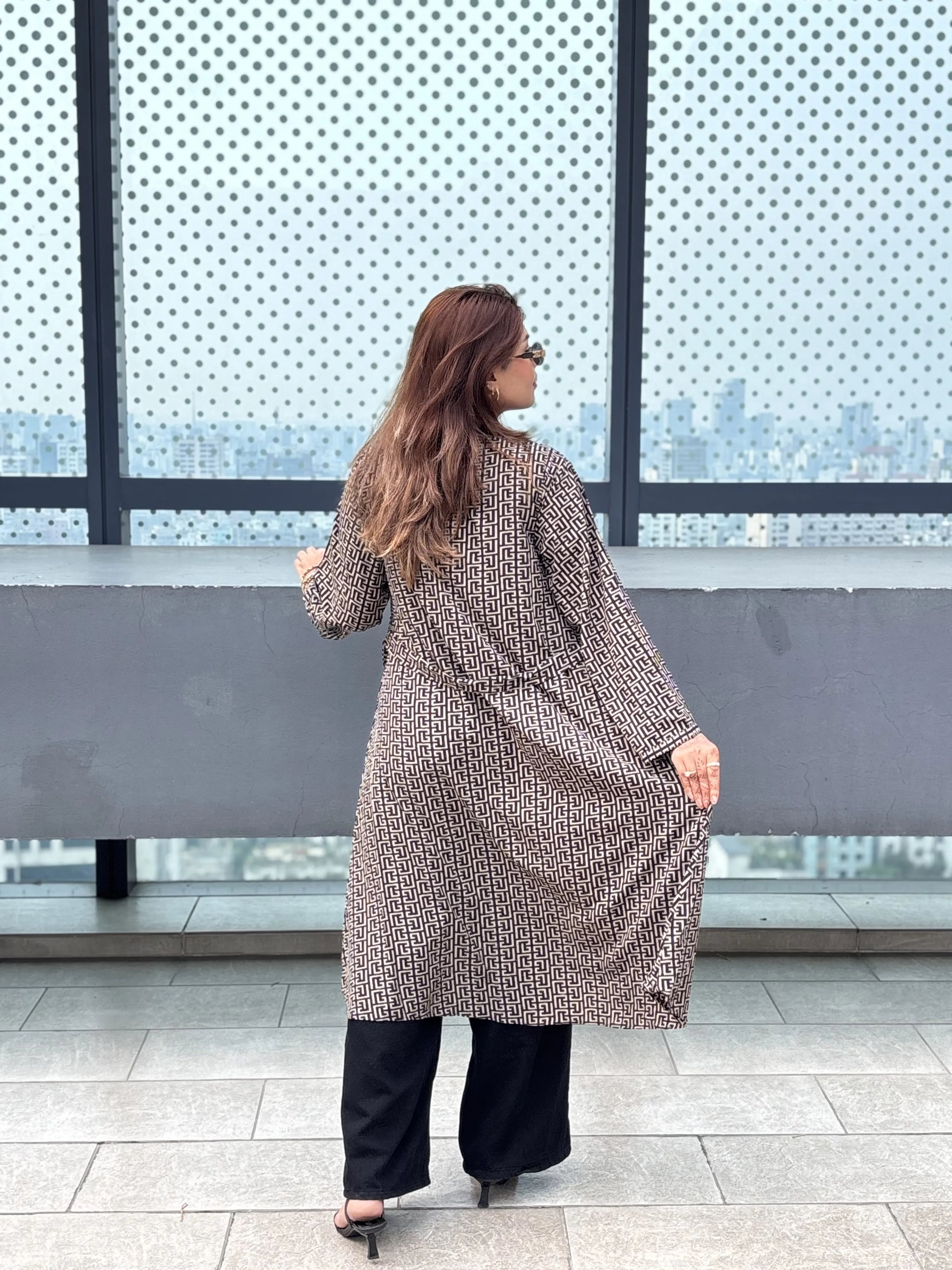 Woman in a patterned Shrug standing in front of large windows with a cityscape view.