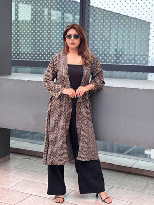 Woman in a long patterned Shrug and black pants standing in front of a modern building.