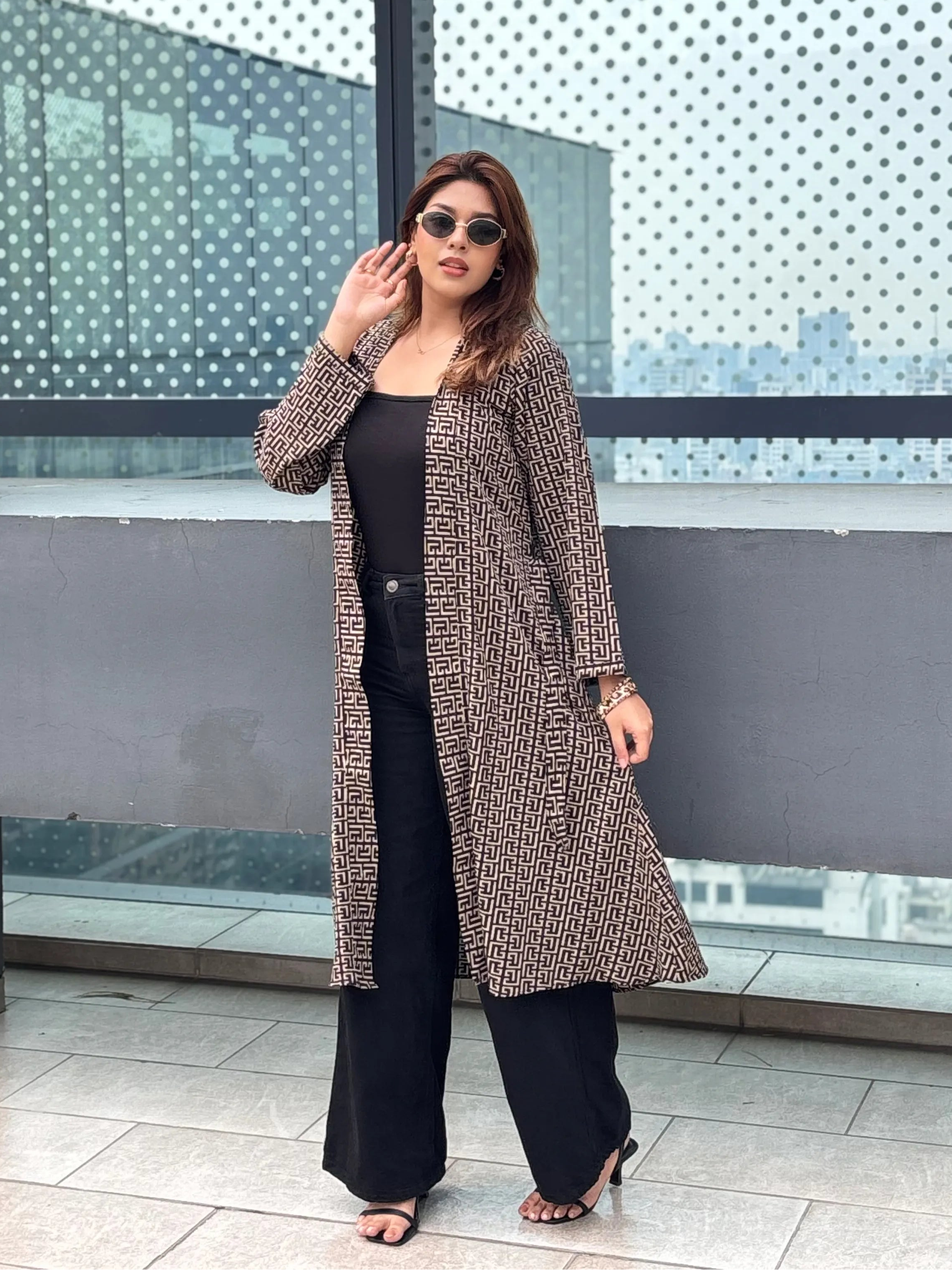 Woman wearing a patterned Shrug and sunglasses standing in front of a modern architectural background.