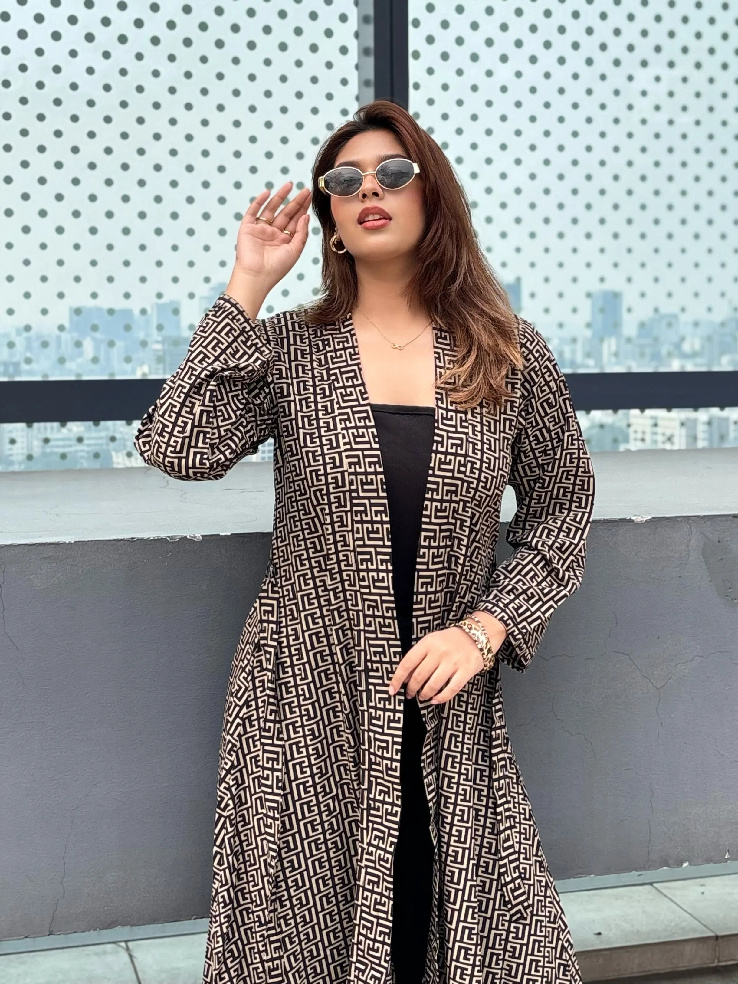 Woman wearing a patterned Shrug and sunglasses in front of a textured wall.