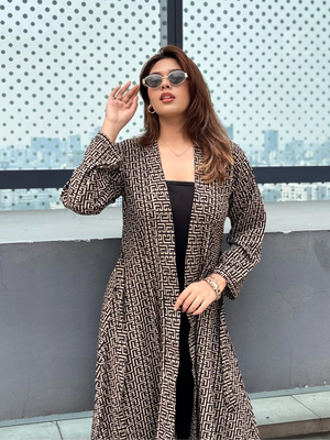 Woman wearing a patterned Shrug and sunglasses in front of a textured wall.