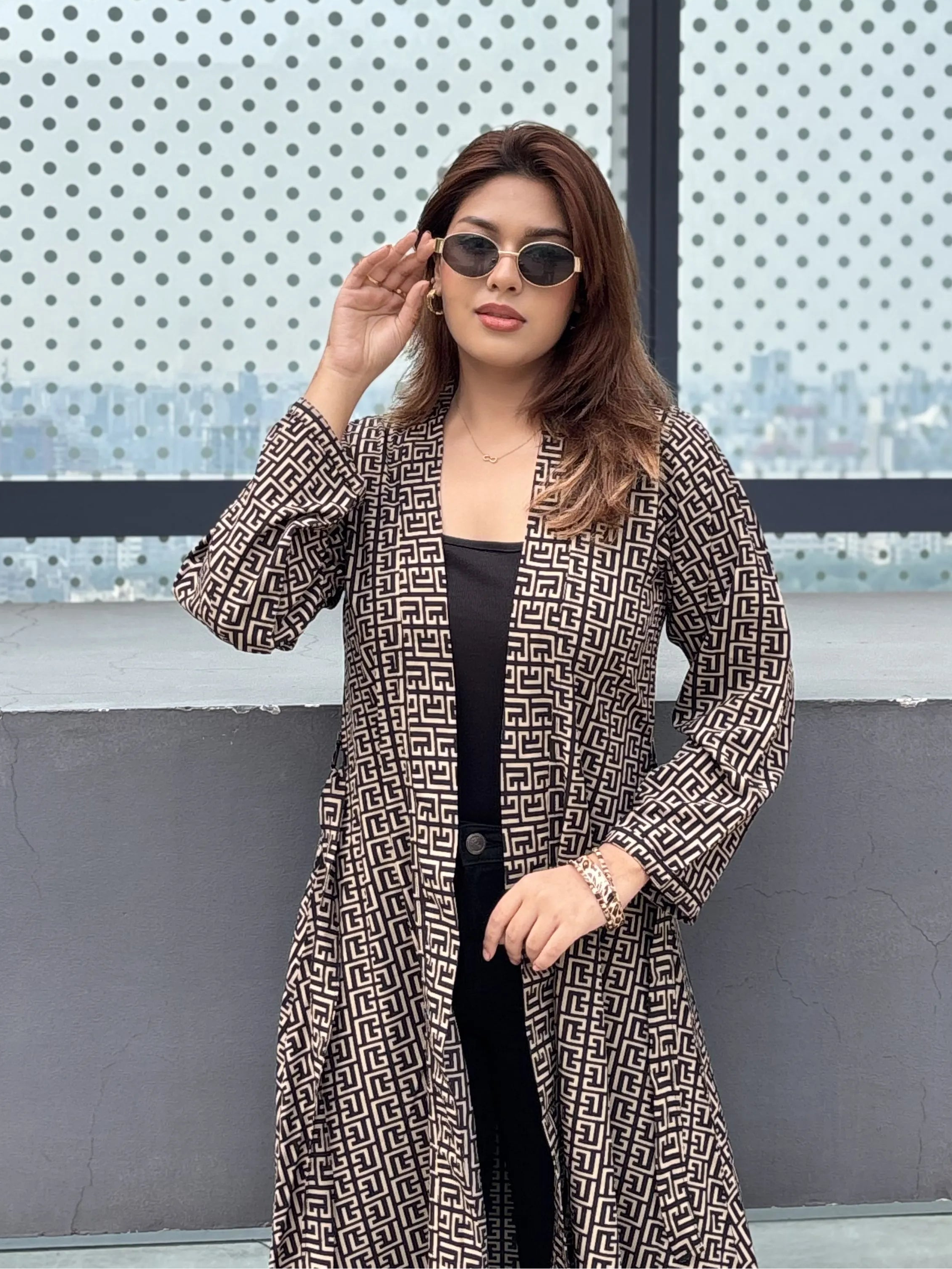 Woman wearing a patterned Shrug and sunglasses against a cityscape background