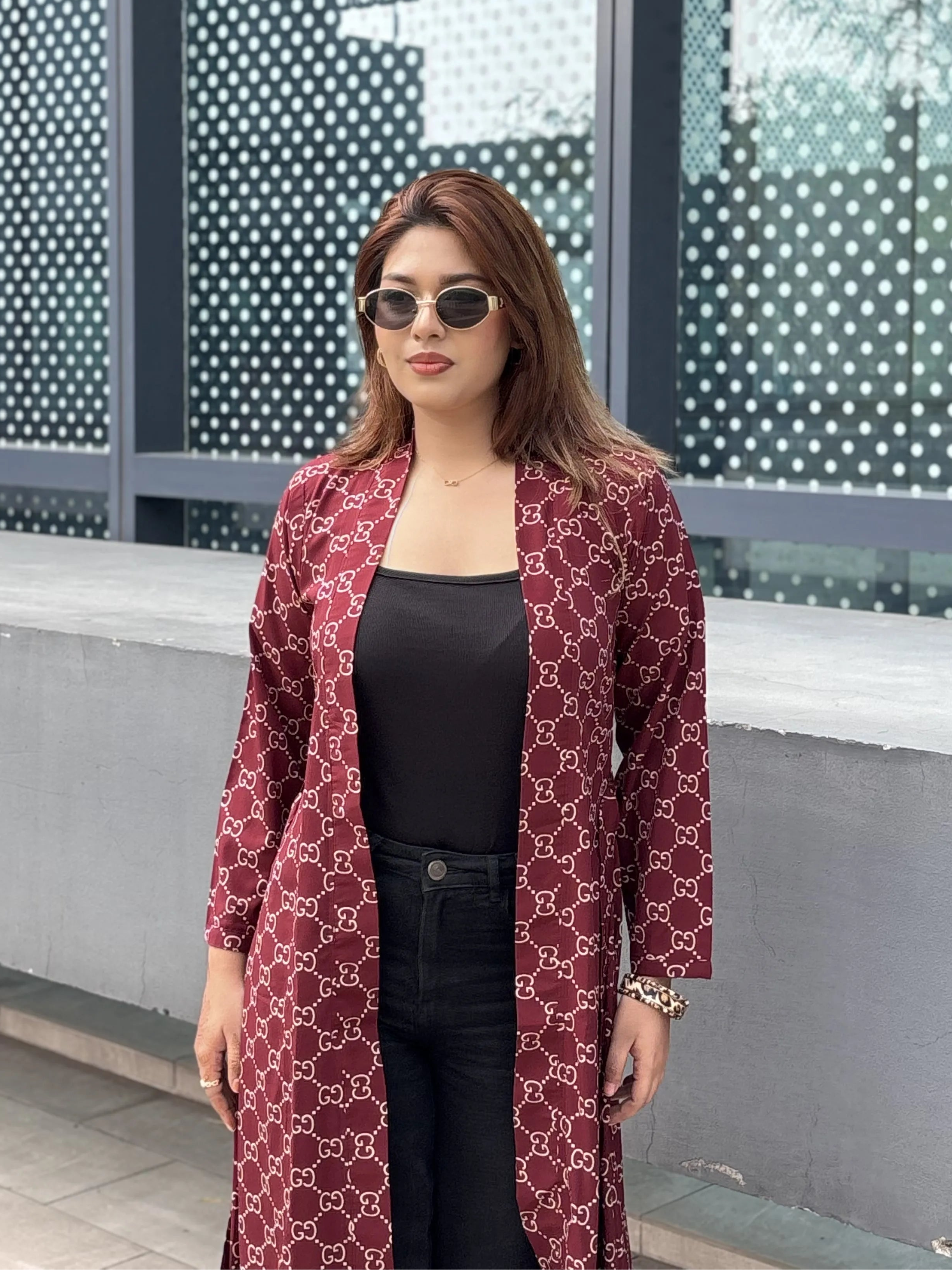 Woman wearing a patterned red Shrug and sunglasses standing in front of a modern building.