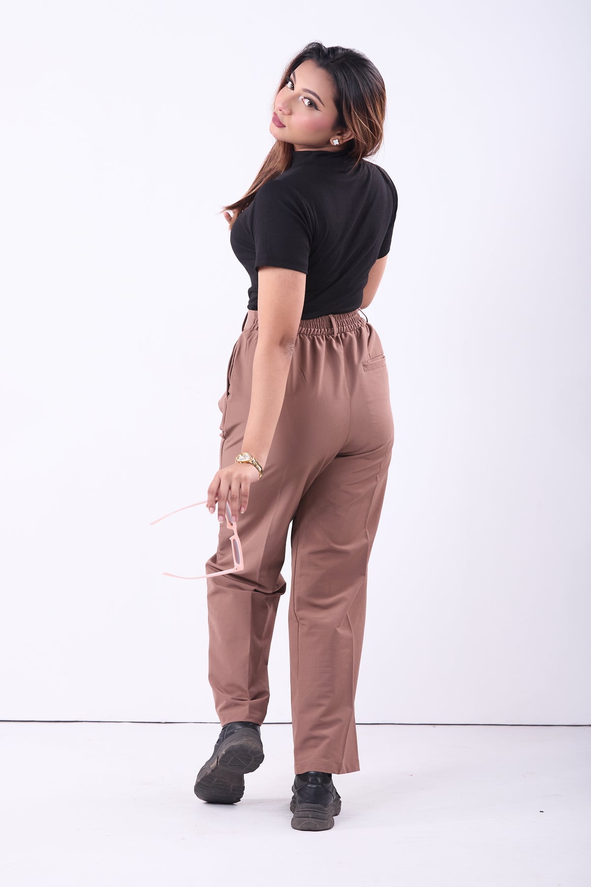 Woman wearing a black top and brown pants on a white background