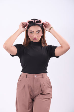 Woman wearing a black top and brown pants with sunglasses on a white background