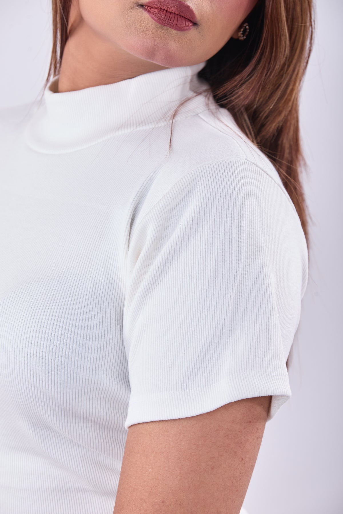 Close-up of a person wearing a white ribbed t-shirt on a plain background