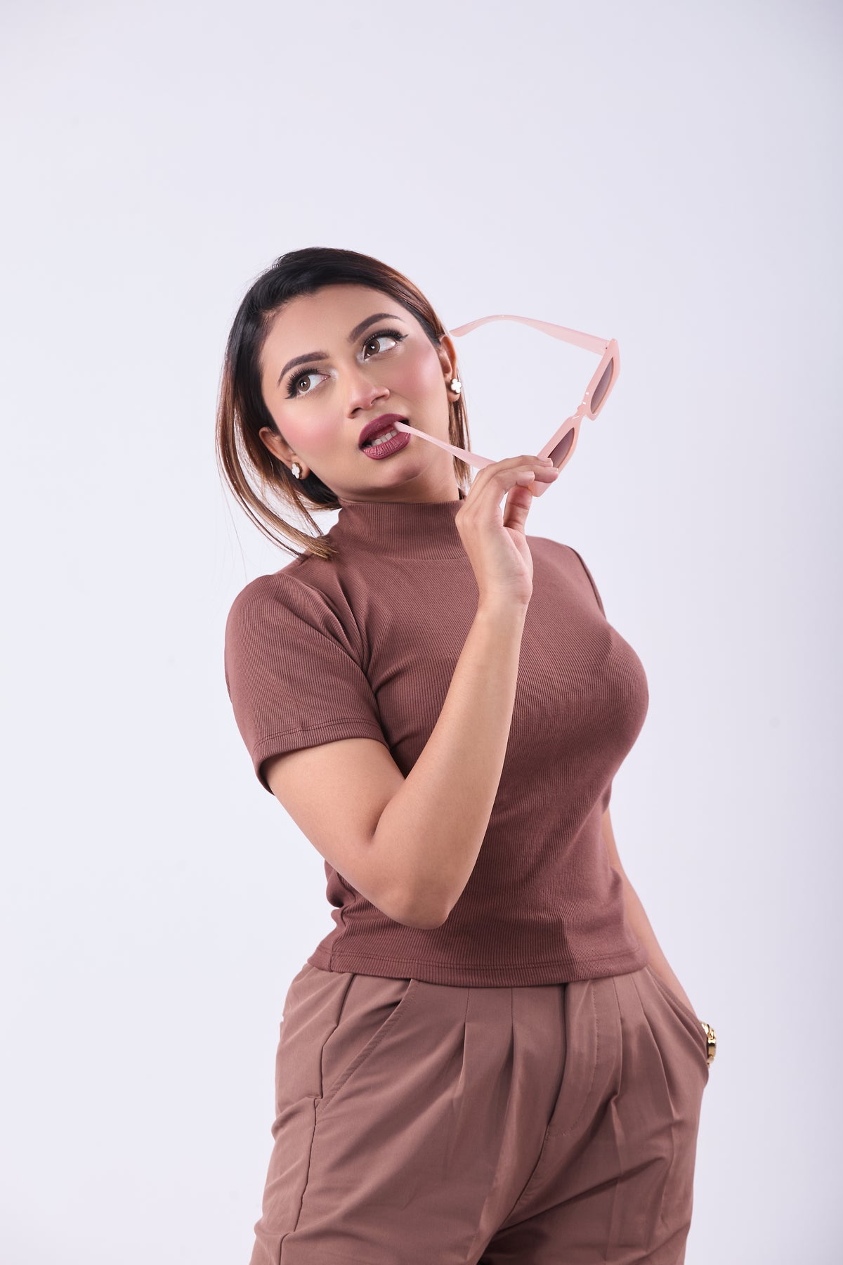 Woman wearing a brown outfit holding a pink heart-shaped object against a white background
