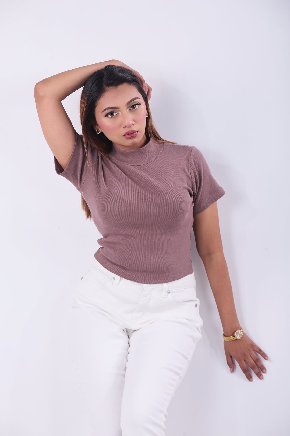 Woman wearing a mauve top and white pants against a white background