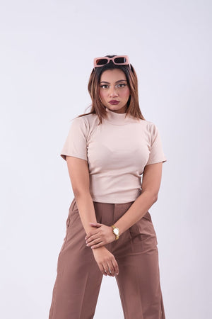 Woman wearing a beige top and brown pants against a white background