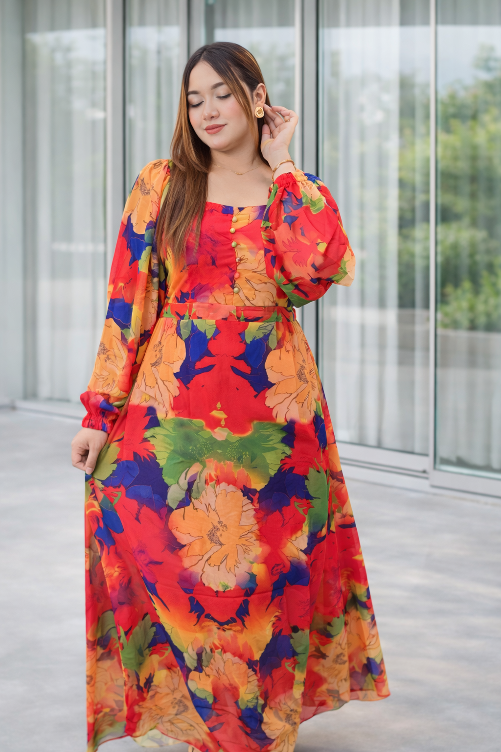 Woman wearing a colorful floral dress standing indoors with a glass wall background