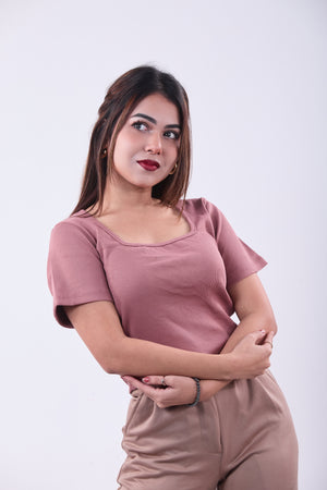 Woman wearing a pink top and beige pants against a white background