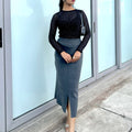 Woman wearing a black top and gray skirt standing in front of glass doors.