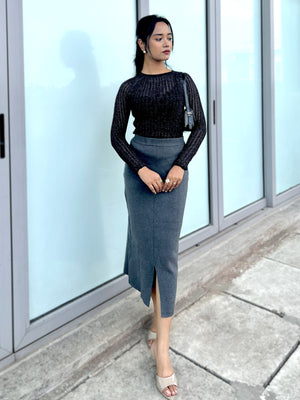 Woman wearing a black top and gray skirt standing in front of glass doors.