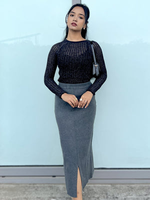 Woman wearing a black top and gray skirt against a light blue wall.