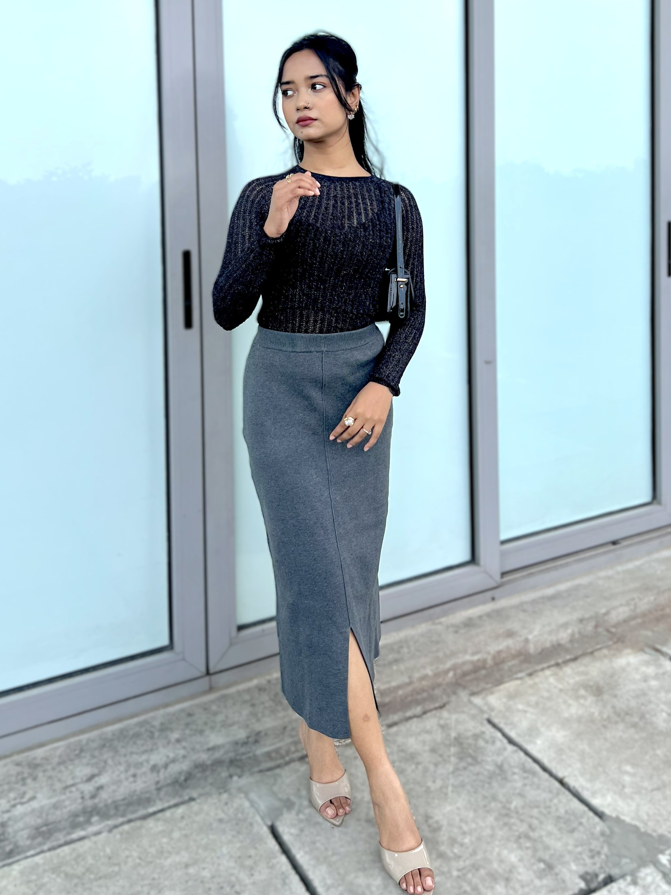 Woman wearing a party top and gray skirt standing in front of glass doors.
