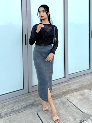 Woman wearing a party top and gray skirt standing in front of glass doors.