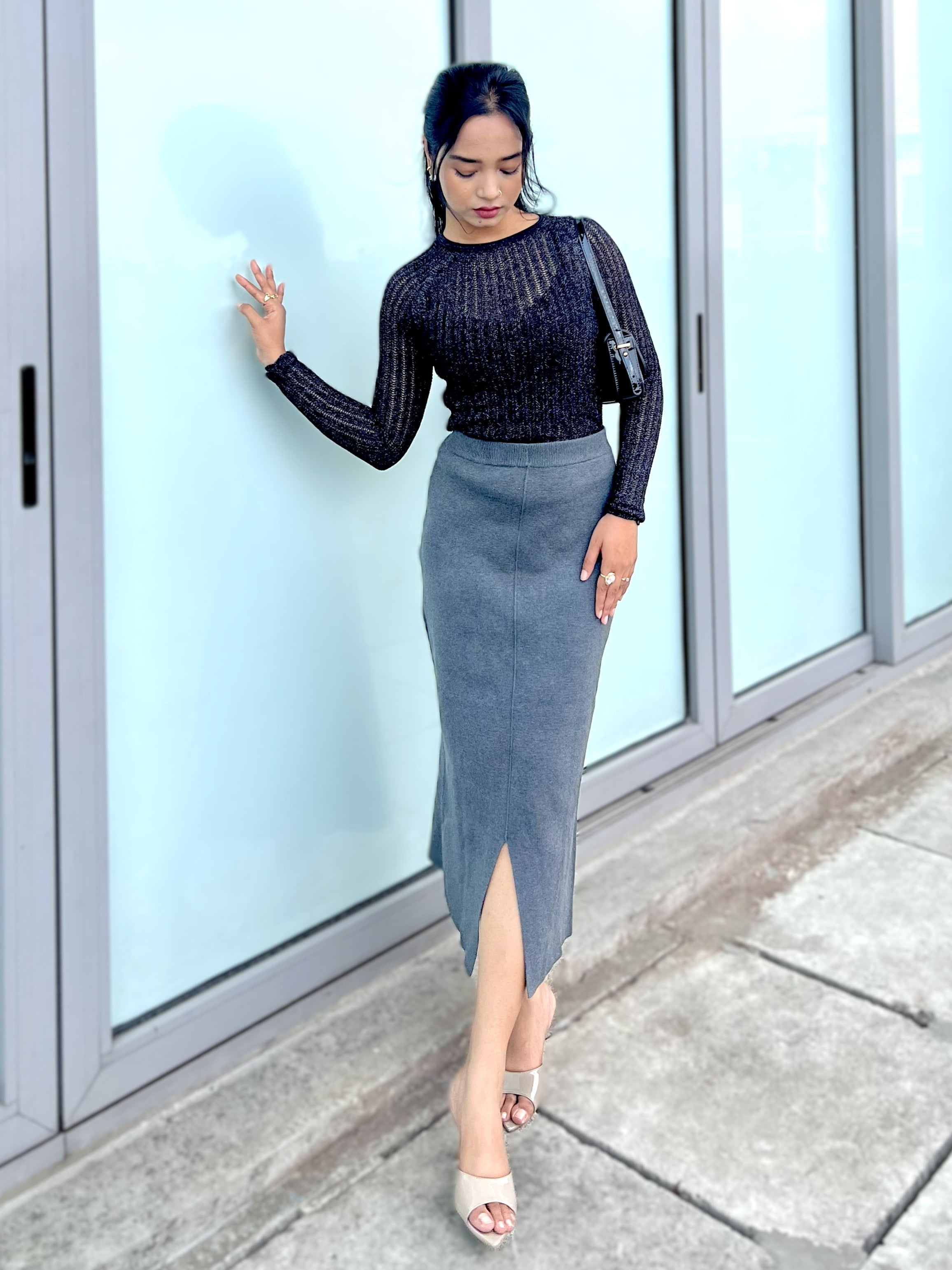 Woman in a black top and gray skirt standing in front of a glass door.