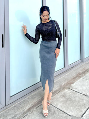 Woman in a black top and gray skirt standing in front of a glass door.