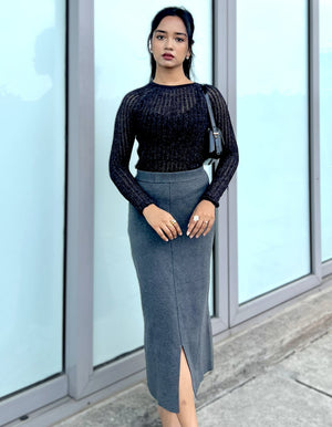 Woman wearing a black glittery mesh top and gray pencil skirt standing in front of glass doors.