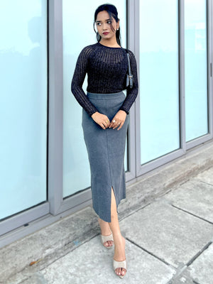 Woman wearing a black top and gray skirt standing outside a building with glass doors.