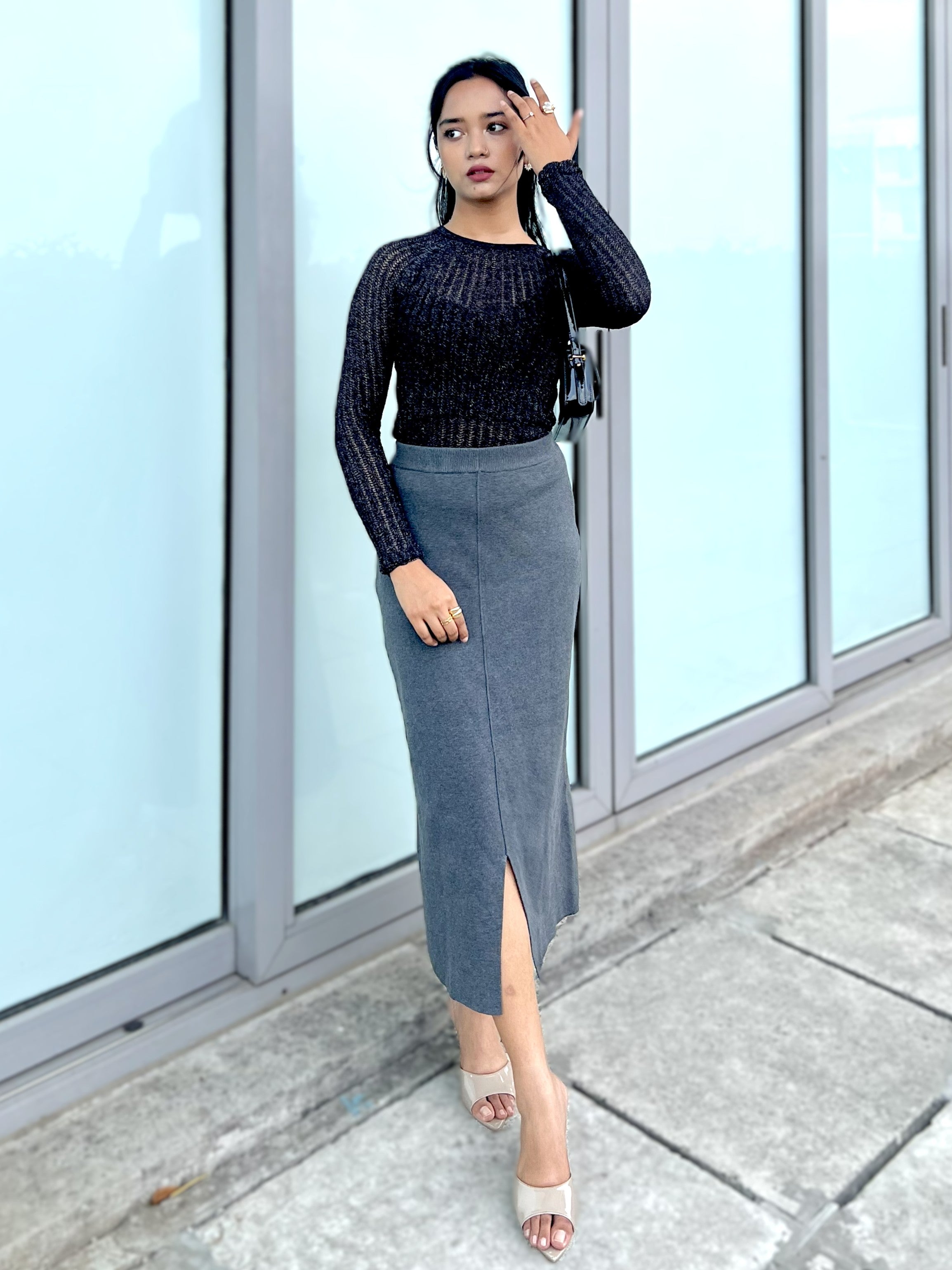 Woman wearing a black glitter attatched top and gray pencil skirt standing in front of glass doors.