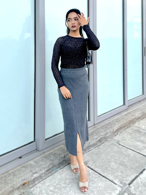 Woman wearing a black glitter attatched top and gray pencil skirt standing in front of glass doors.
