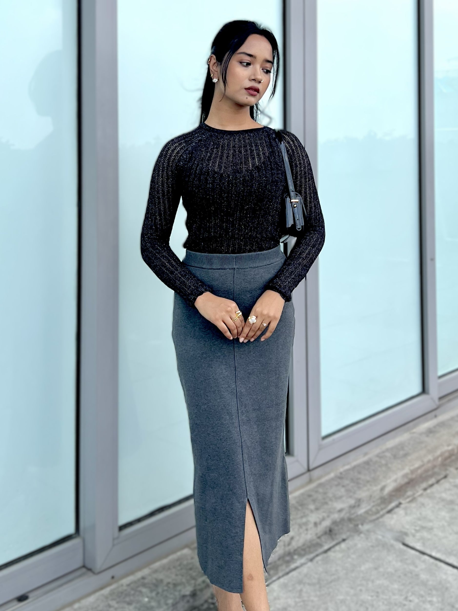 Woman wearing a black party top and gray skirt standing in front of glass doors.