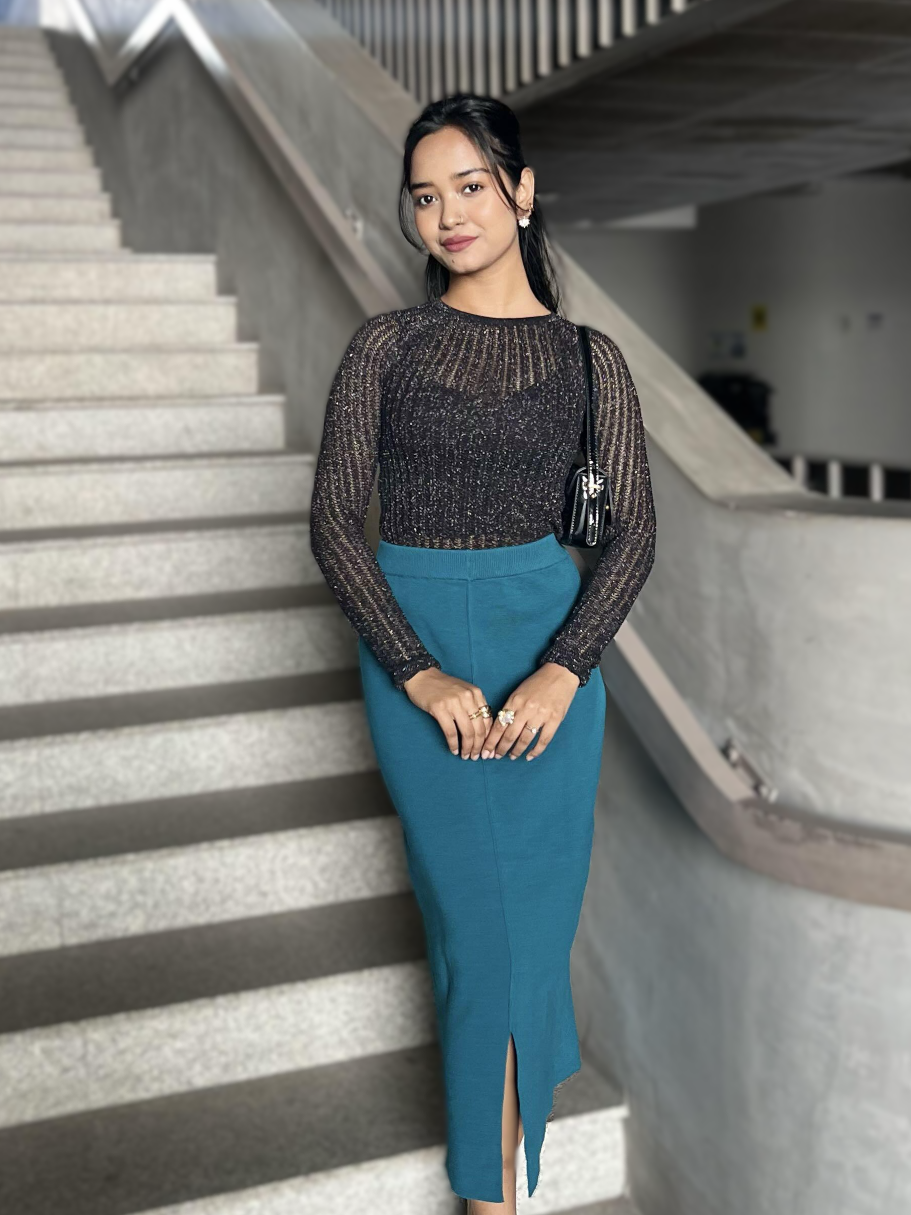Woman in a black party top top and teal or sea blue skirt standing on a staircase.