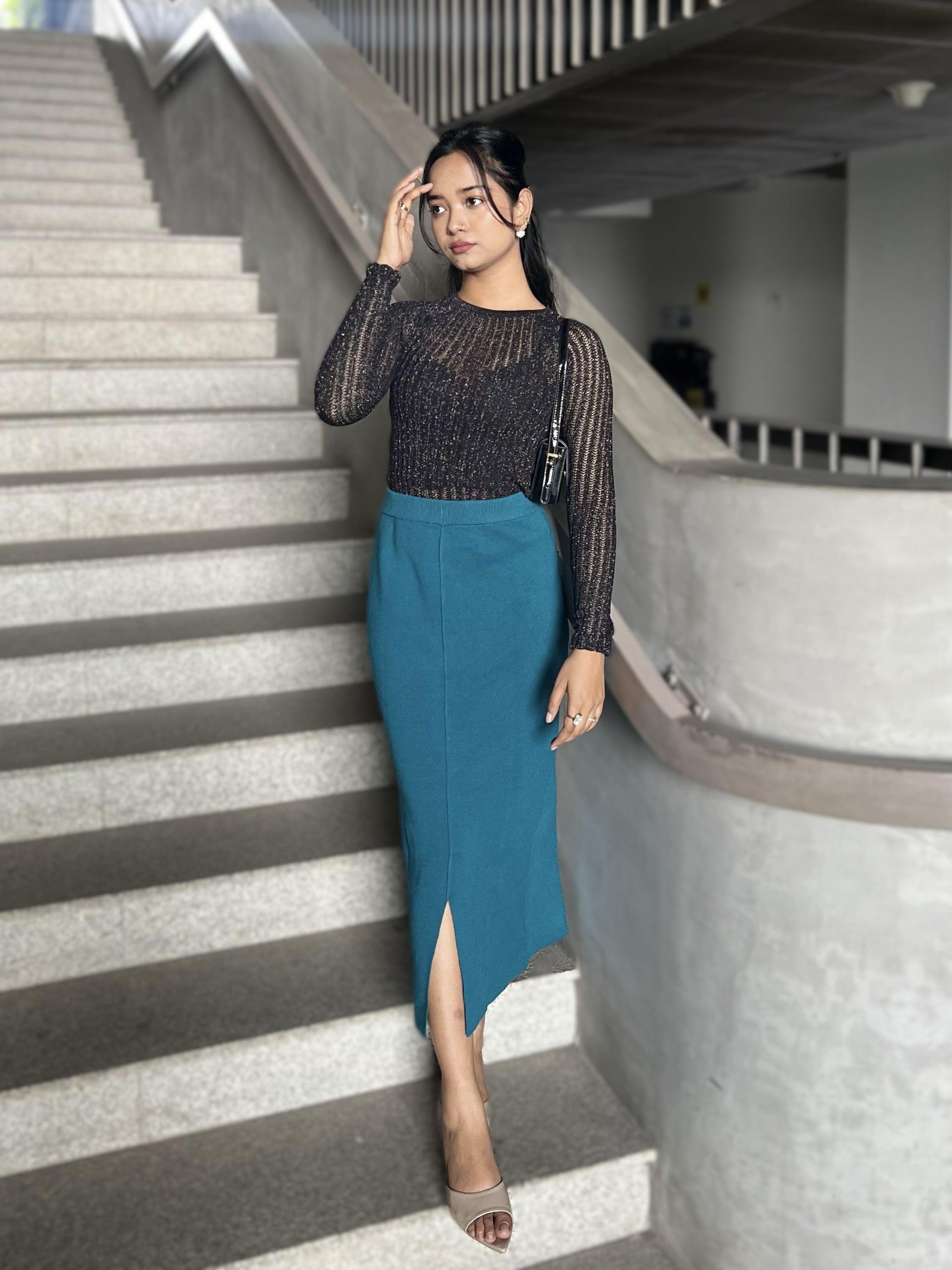 Woman in a black top and blue skirt standing on a staircase.