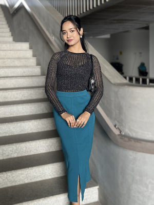 Woman in a black glittery top and sea blue skirt standing on a staircase.