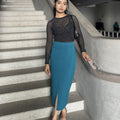 Woman in a black top and teal skirt standing on a staircase.