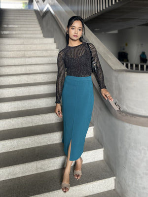 Woman in a black top and teal skirt standing on a staircase.