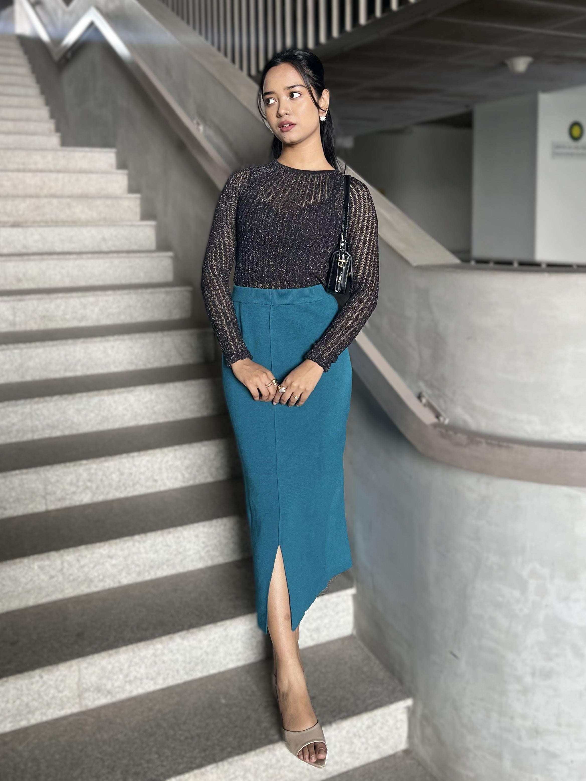 Woman in a black top and blue skirt standing on a staircase indoors.