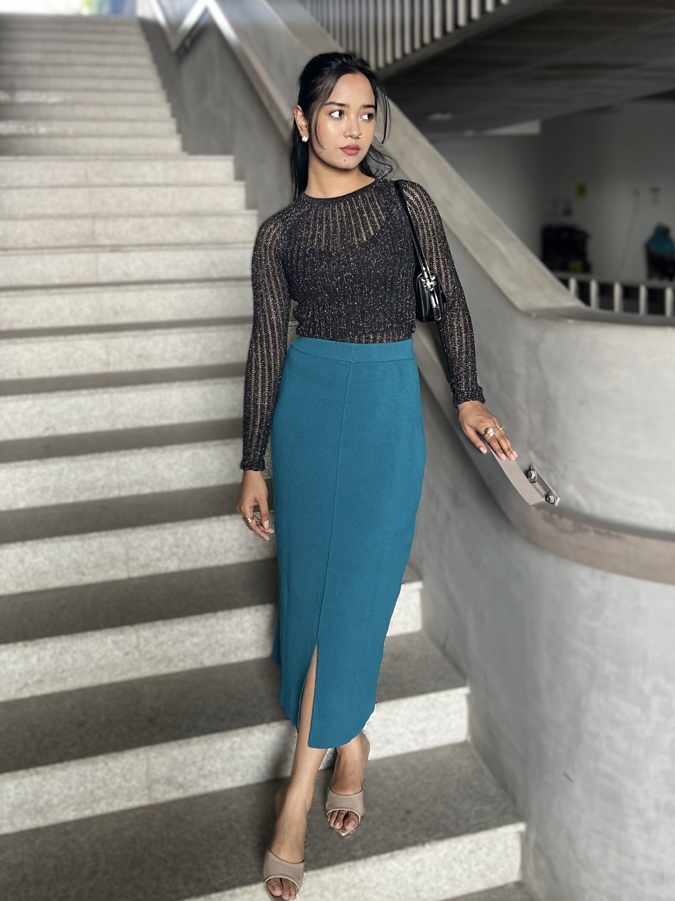 Woman in black top and teal skirt standing on a staircase