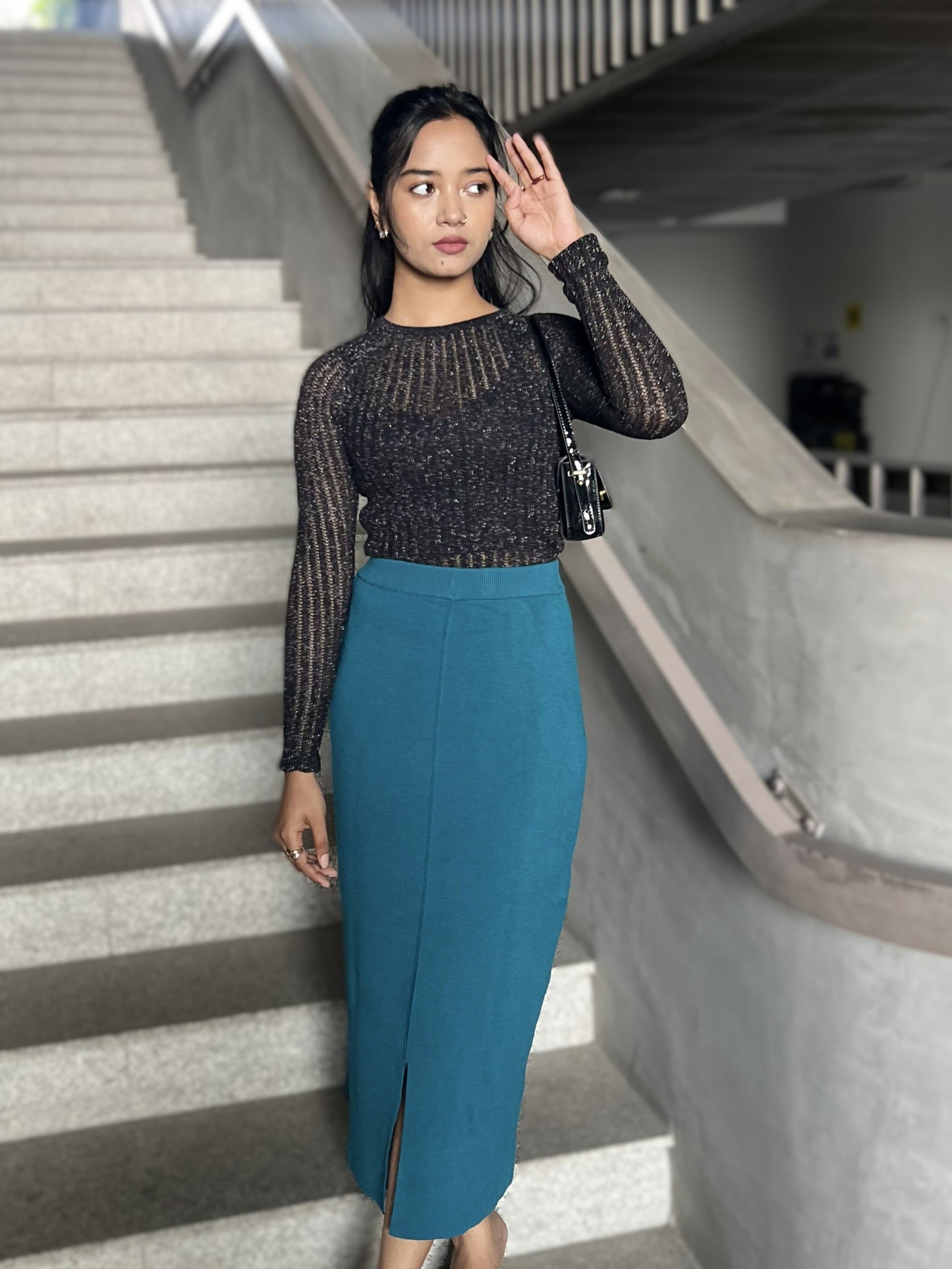 Woman in a black top and sea blue skirt standing on a staircase.