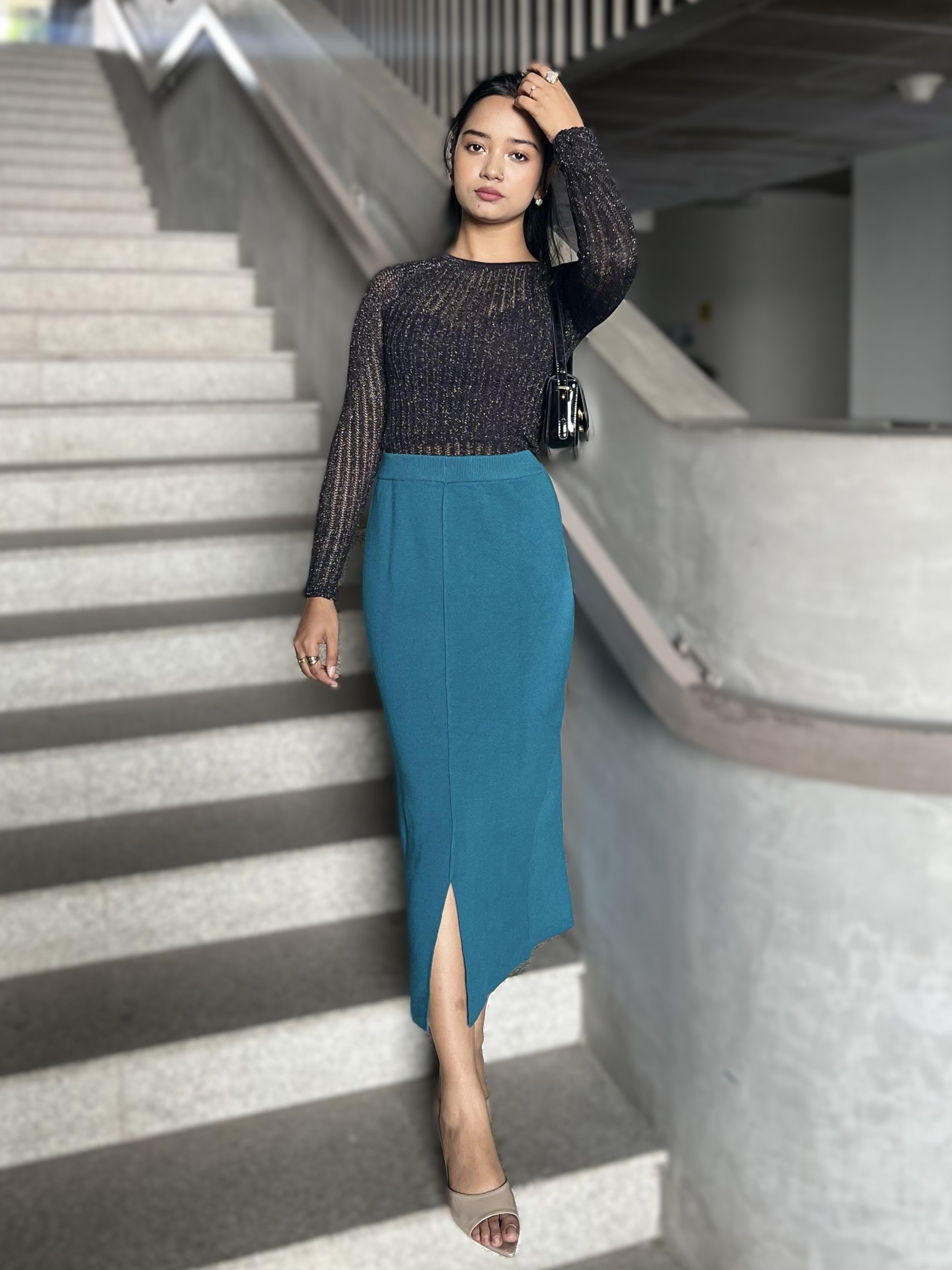Woman in a black top and teal skirt standing on a staircase.