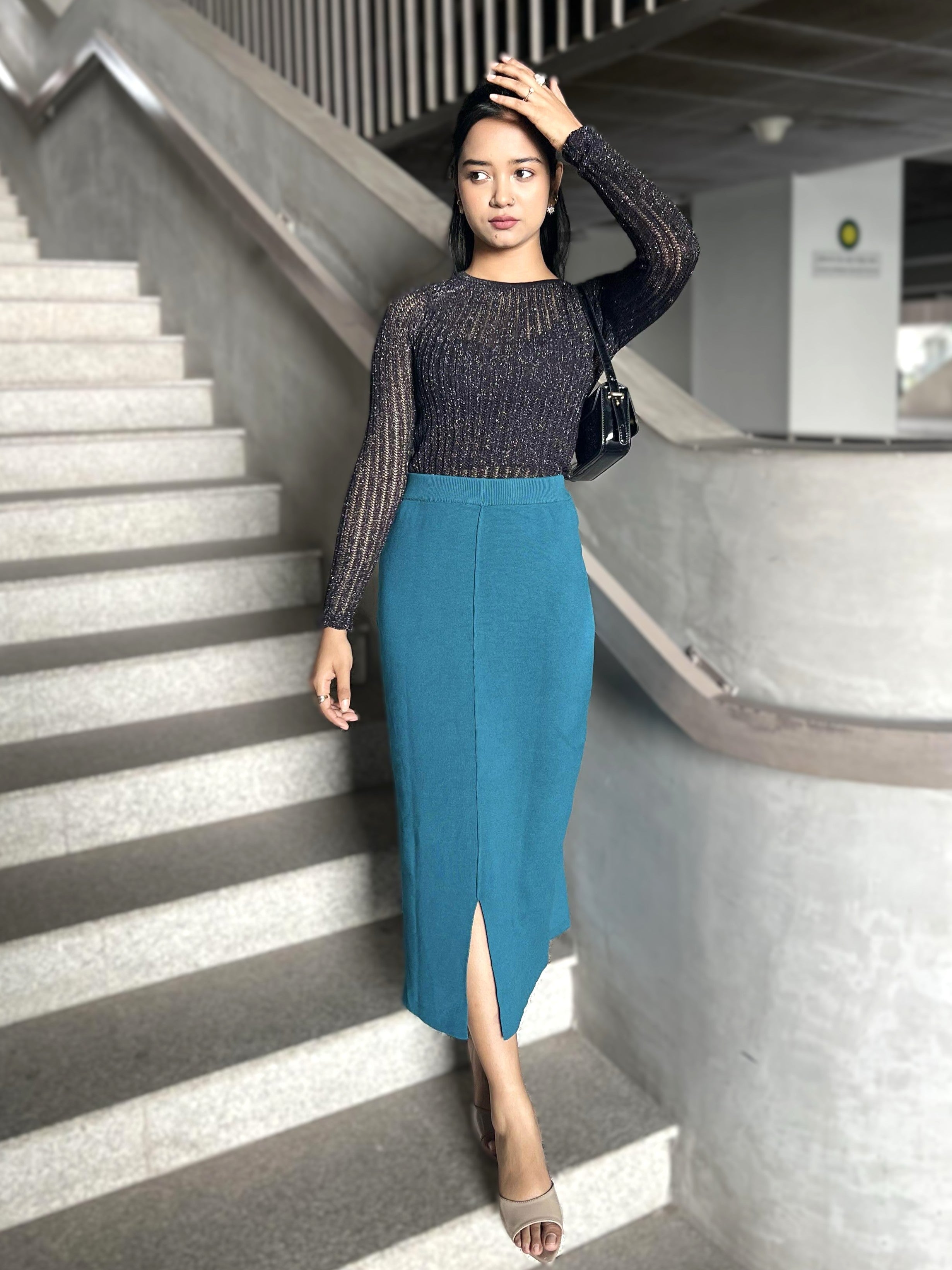 Woman in a blue skirt and black top standing on a staircase.