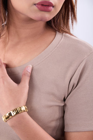 Close-up of a person wearing a beige top and gold bracelet.