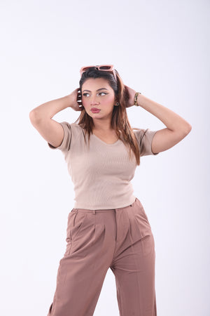 Woman wearing a beige top and brown pants with sunglasses on her head against a white background