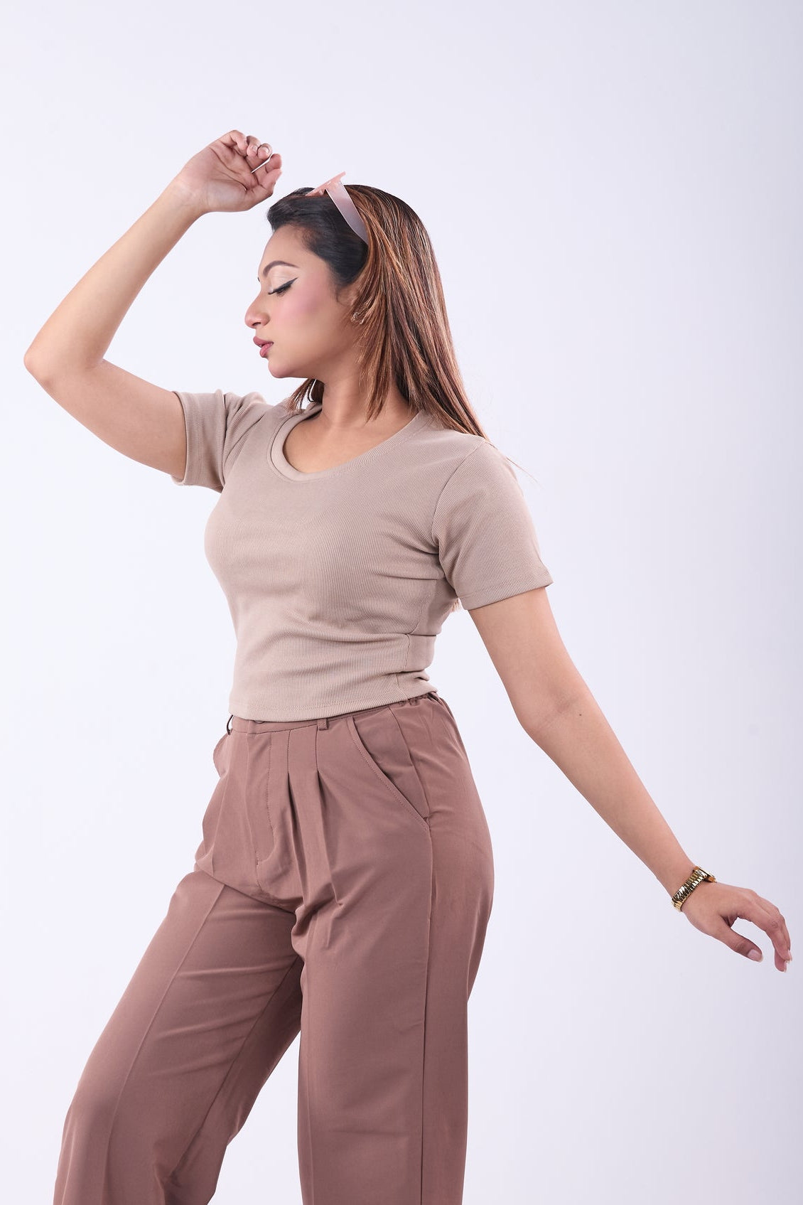 Woman wearing a beige top and brown pants on a white background