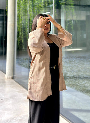 A woman wearing a light beige linen-textured open-front Kimono over a black top and black pants, standing outdoors in front of a modern glass building.