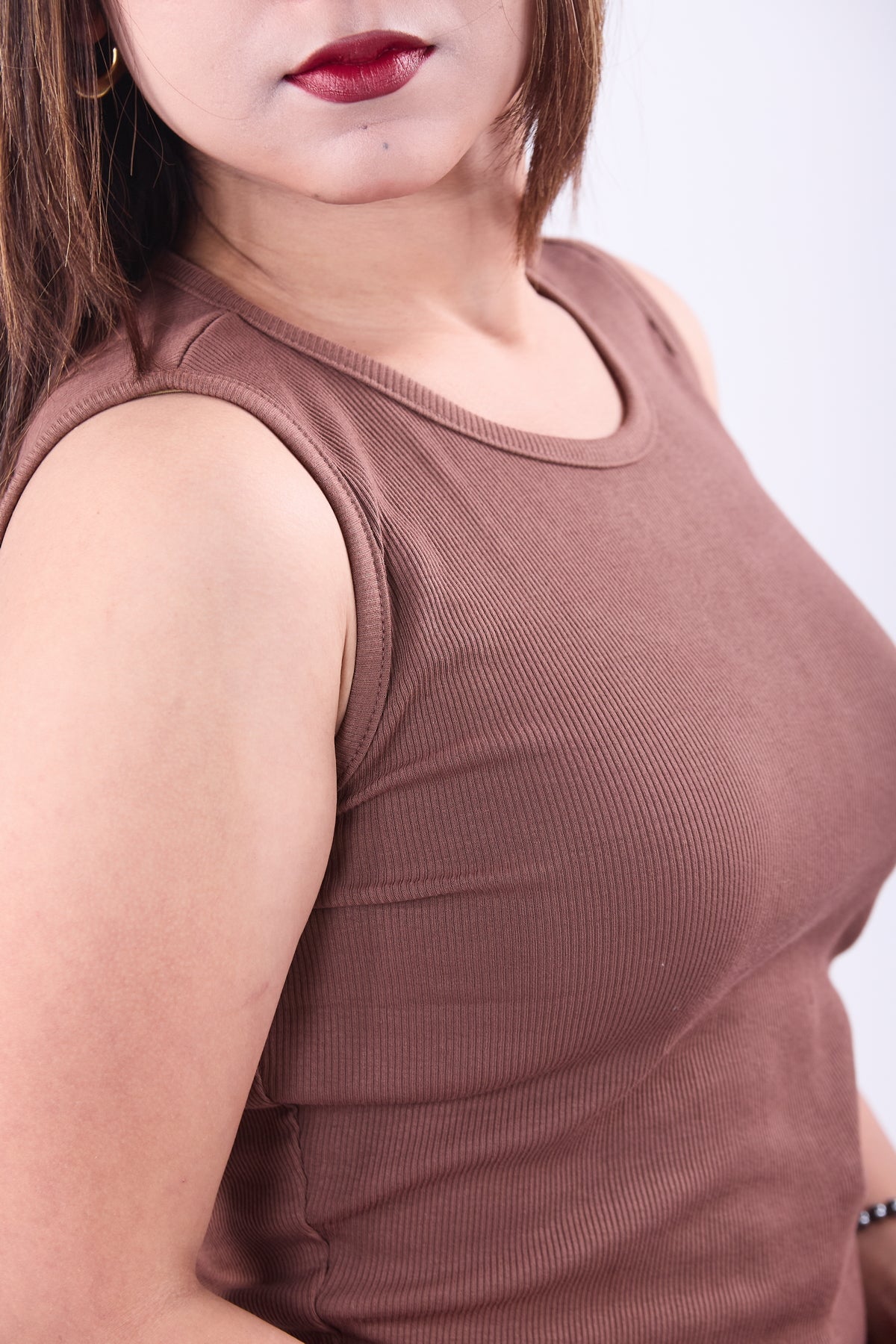 Close-up of a person wearing a brown sleeveless top against a white background
