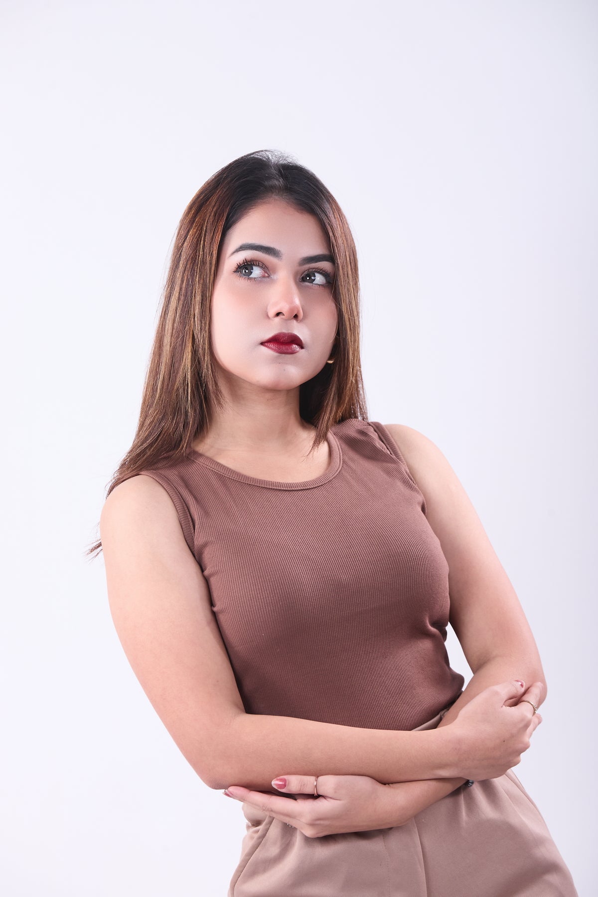 Woman wearing a brown sleeveless top and beige pants against a white background