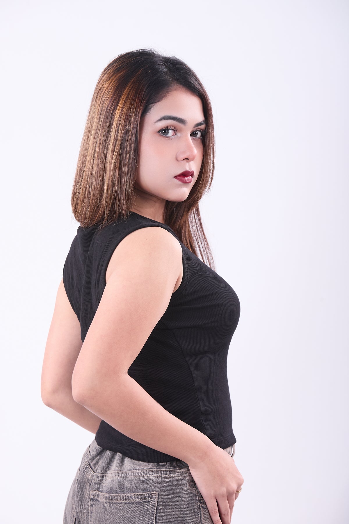 Woman wearing a black sleeveless top and gray pants on a white background