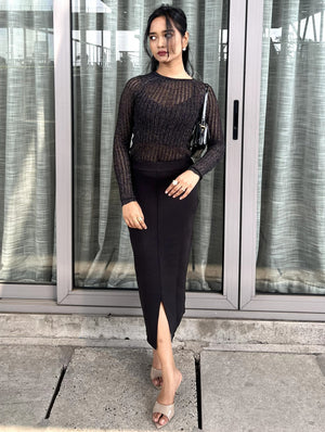 Woman in a black party top & black skirt outfit standing in front of a glass door.