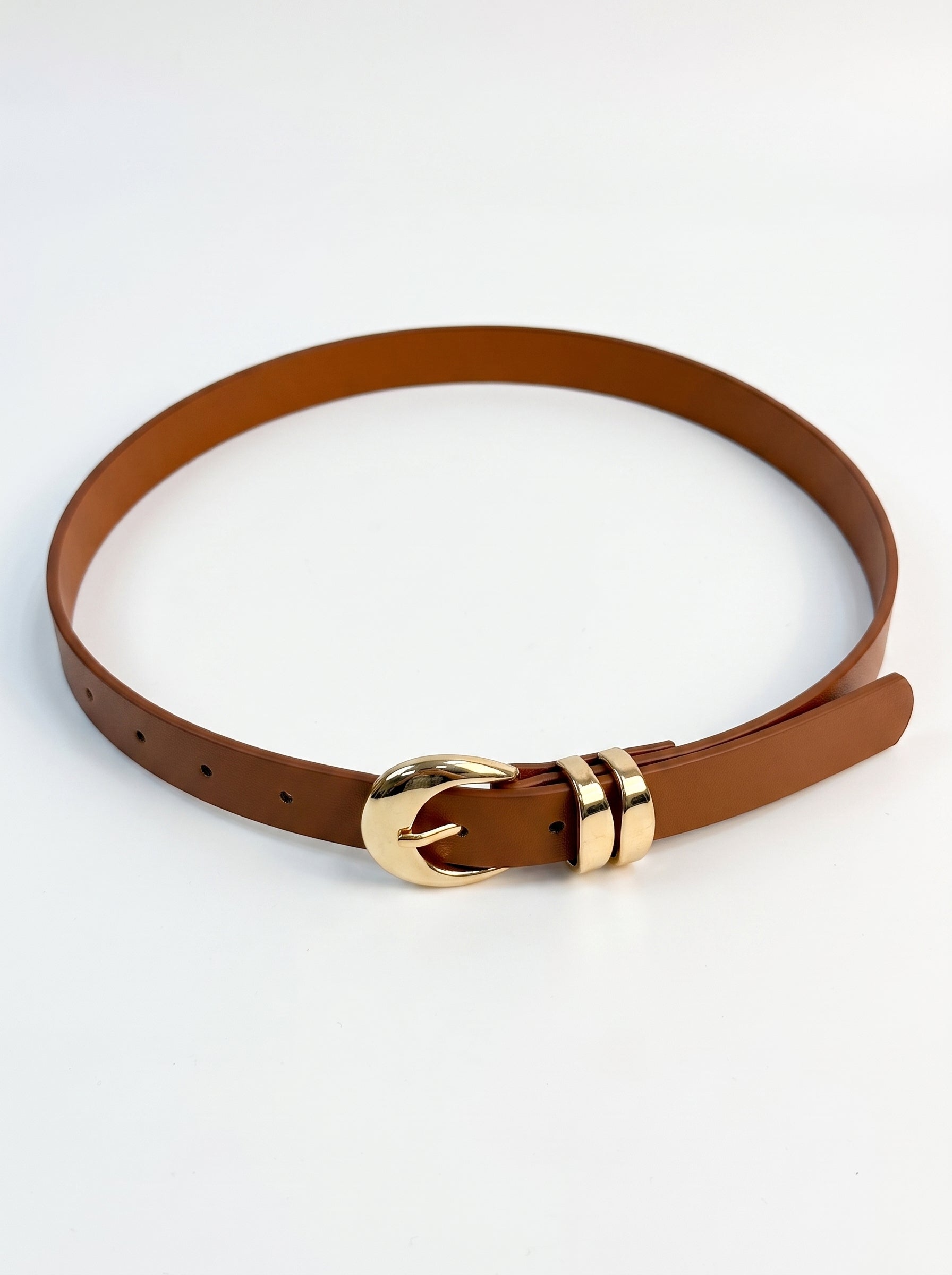 A brown leather belt with a polished gold-tone buckle and matching gold-tone tip, arranged in a loop on a clean white background.