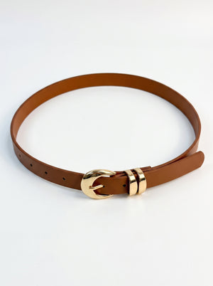 A brown leather belt with a polished gold-tone buckle and matching gold-tone tip, arranged in a loop on a clean white background.