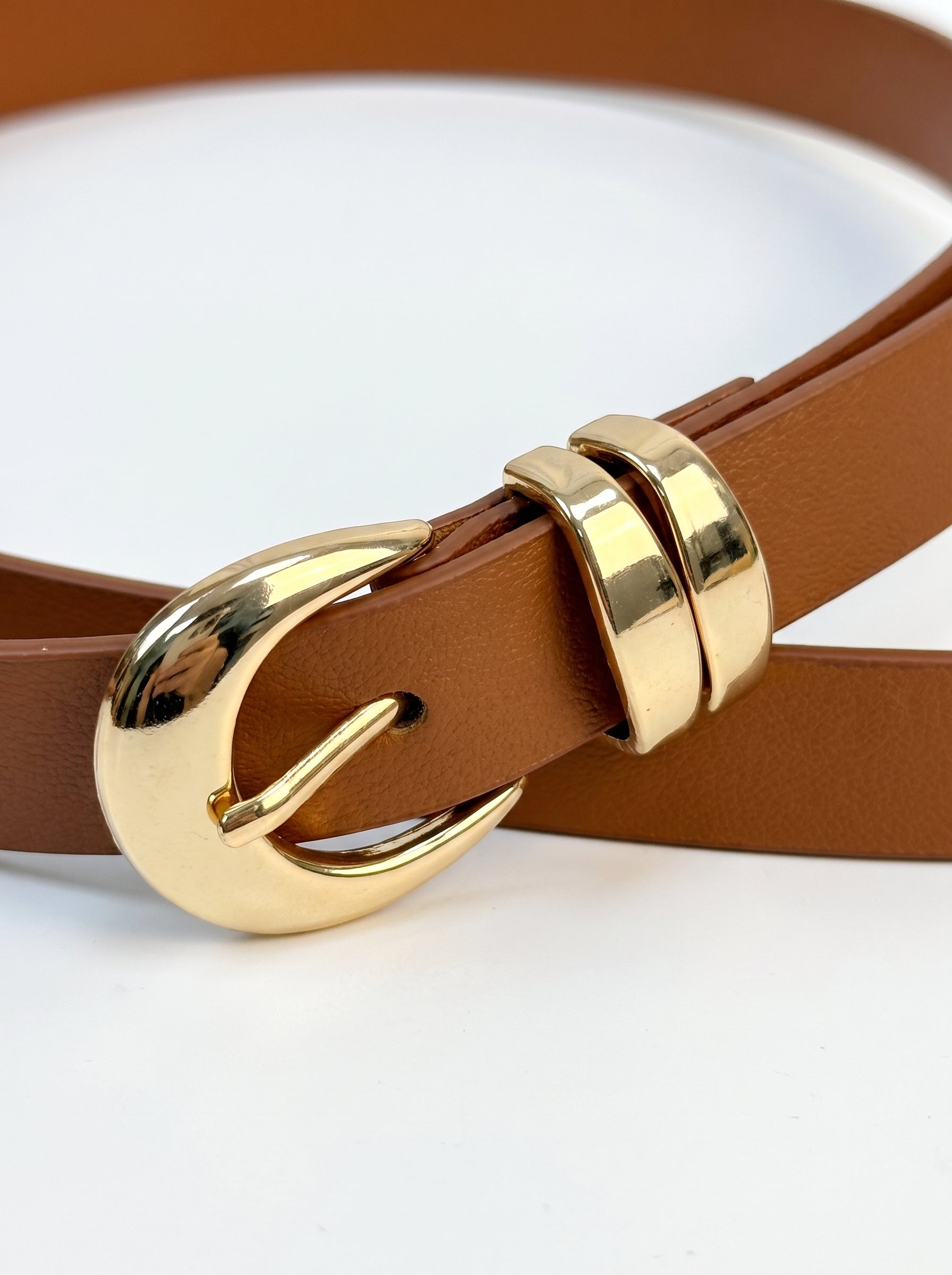 A close-up of a brown leather belt with a polished gold-tone buckle, resting on a clean white background.