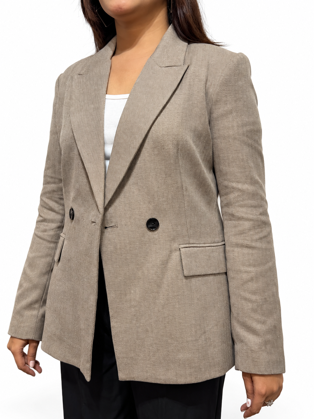 A woman wearing a light taupe double-breasted blazer over a white top and black pants, shown from the neck down against a plain white background.