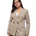 A woman wearing a light beige double-breasted blazer over a white top and black trousers, standing against a plain white studio background.